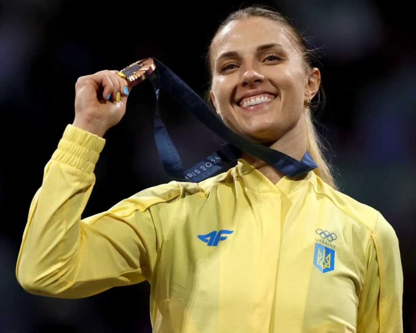 Ольга Харлан в жовтій спортивній кофті тримає золоту медаль після перемоги в фехтуванні