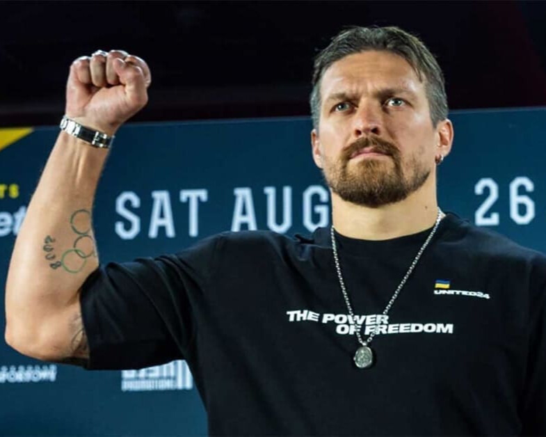 Олександр Усик з піднятим кулаком у чорній футболці з написом 'the power of freedom' перед боєм, під час зіткнення поглядами