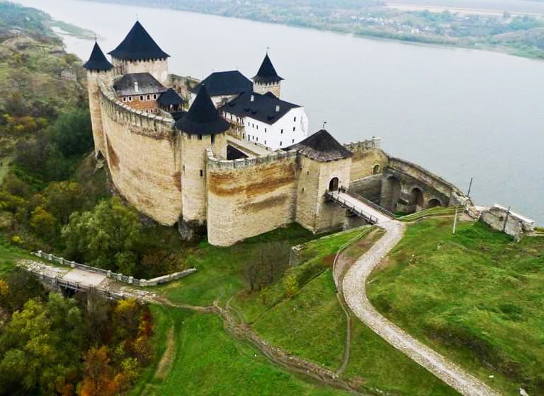  Вид з висоти на замок, що стоїть на березі річки, оточений природою.