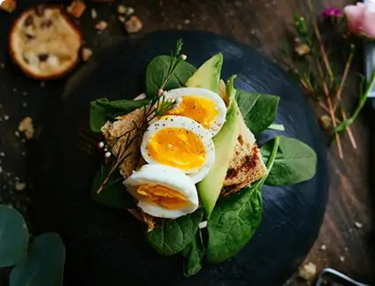 Sliced avocado and poached eggs atop a slice of toasted bread, garnished with herbs.