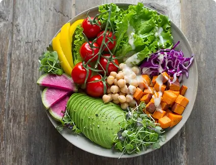 A vibrant assortment of vegetables and fruits is arranged in a bowl on a wooden table.